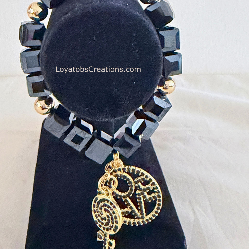 Black cube bead and gold accent bracelet with gold LOVE charm and black crystal lollipop charm on black jewellery stand - LoyatobsCreations.com