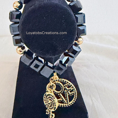 Black cube bead and gold accent bracelet with gold LOVE charm and black crystal lollipop charm on black jewellery stand - LoyatobsCreations.com