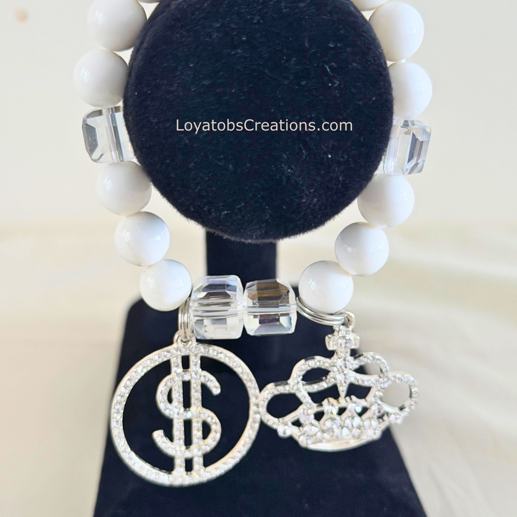 White bead and clear crystal cube bracelet with silver pavé dollar sign and crown charms on black jewellery stand - LoyatobsCreations.com