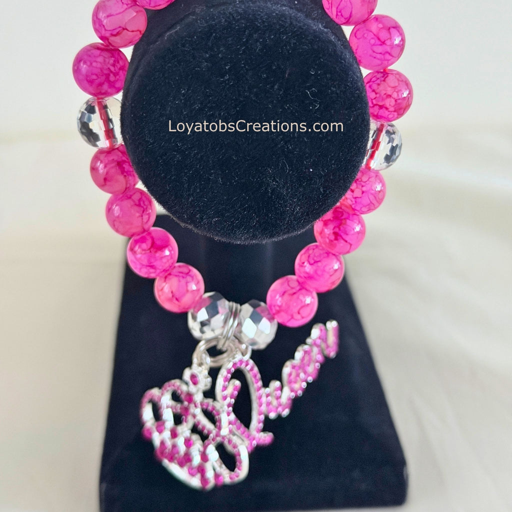 Hot pink crackle bead bracelet with pink rhinestone crown and Queen script charms on black jewellery stand - LoyatobsCreations.com