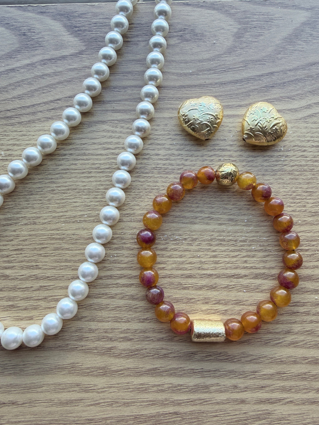 "Lifestyle shot of multi bronze jade bracelet styled with pearl necklace and gold heart accessories on wood surface"