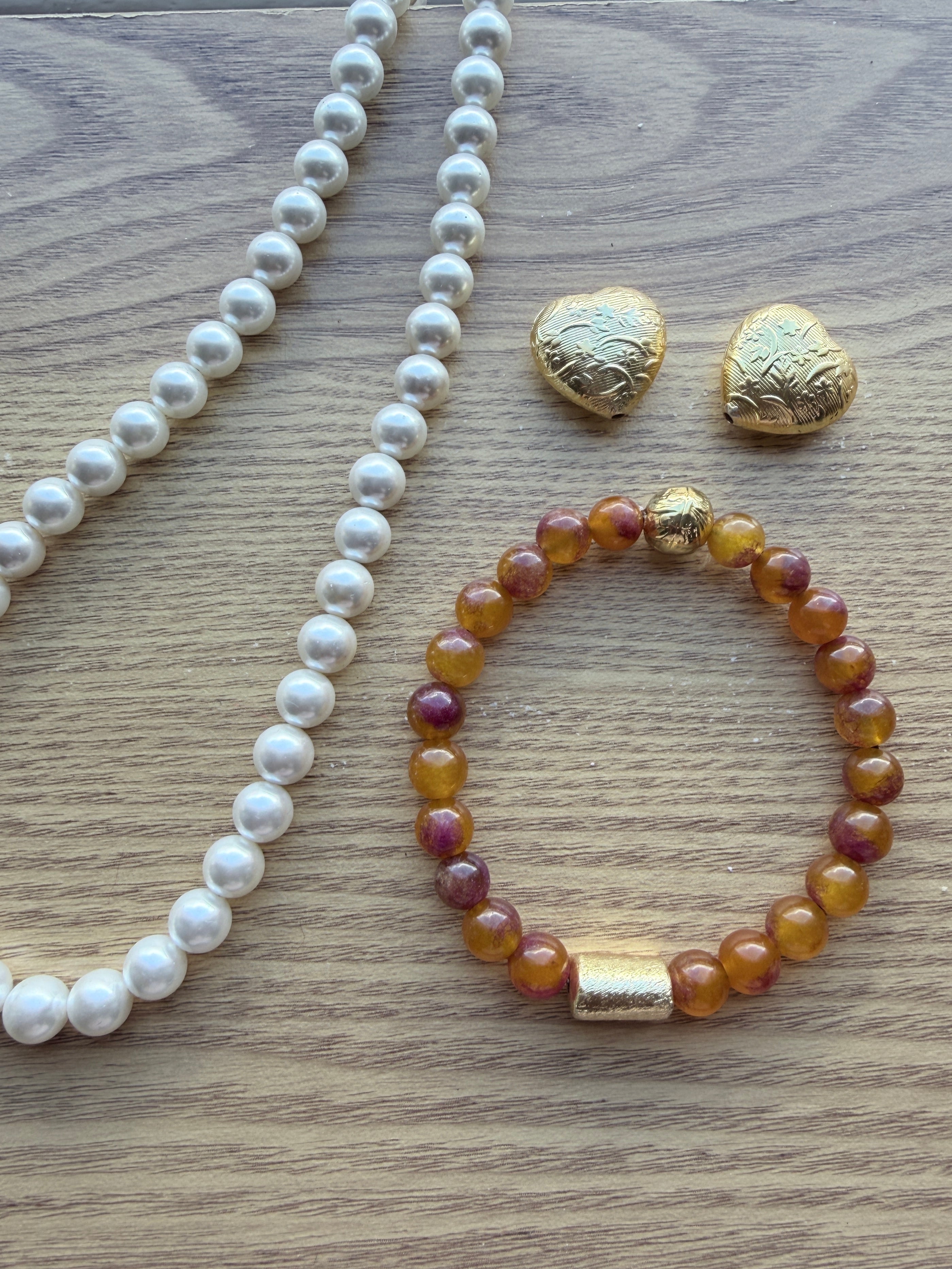 "Lifestyle shot of multi bronze jade bracelet styled with pearl necklace and gold heart accessories on wood surface"
