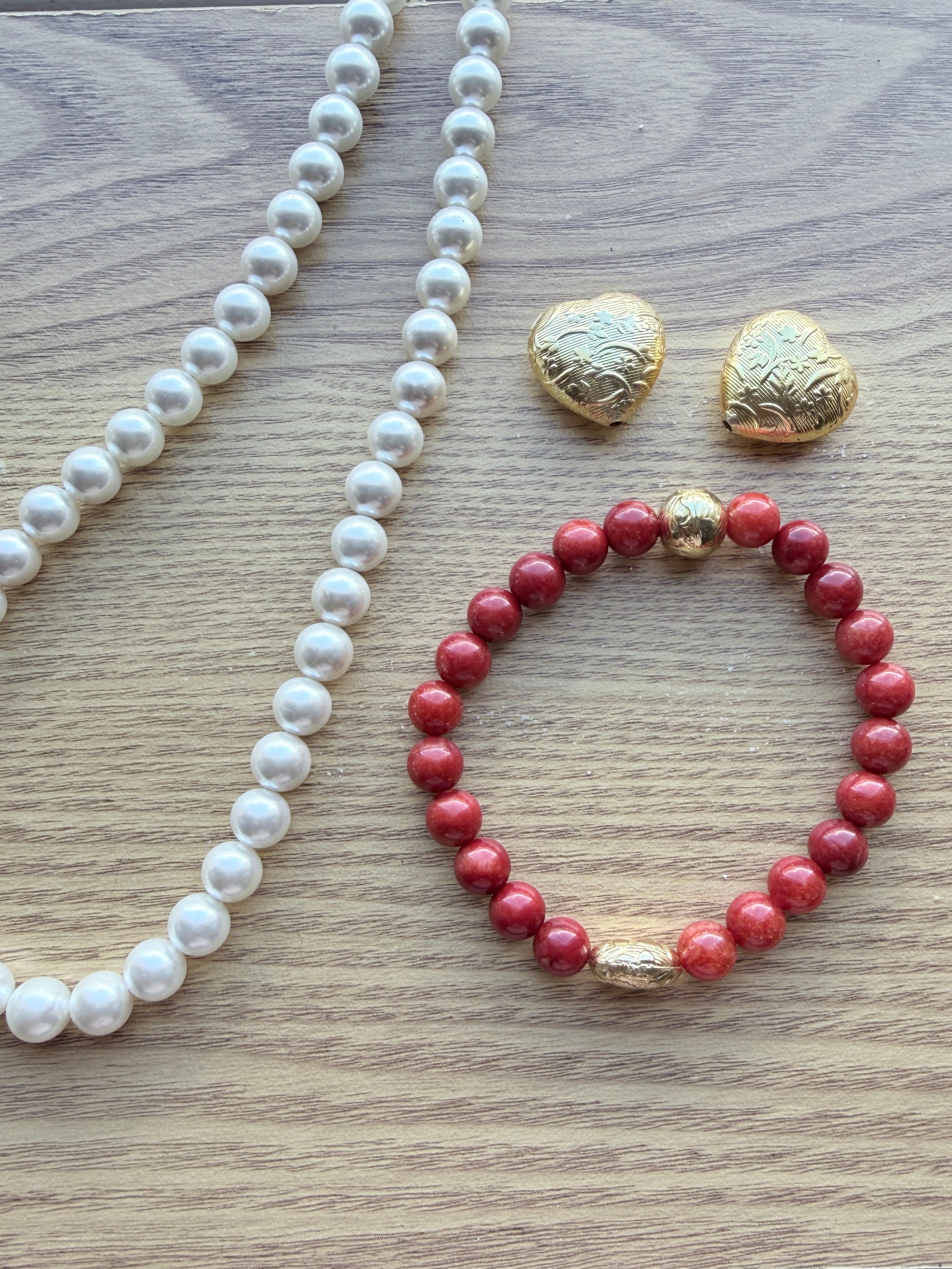 "Lifestyle shot of coral jade bracelet styled with pearl necklace and gold heart accessories on wood surface"