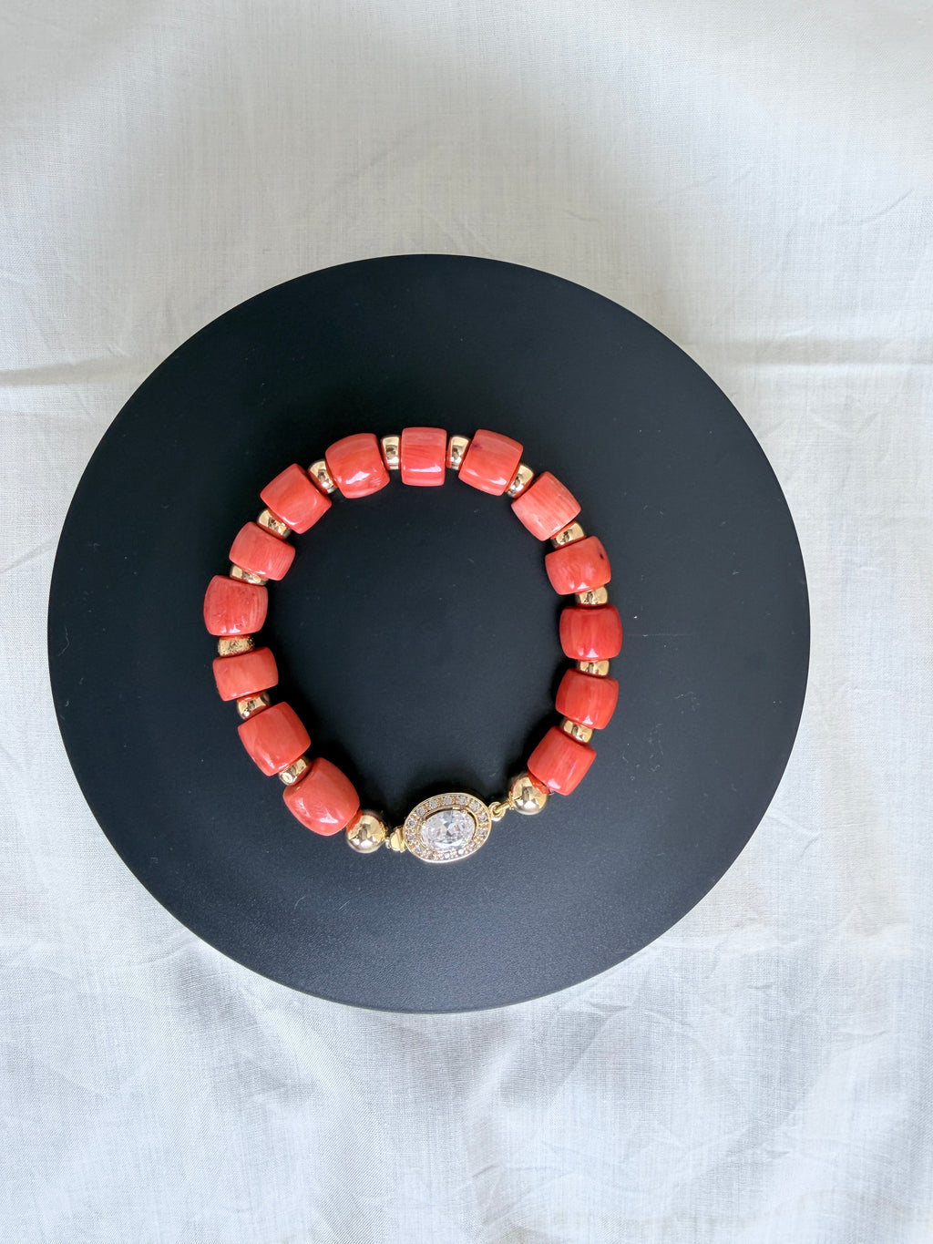 "Coral barrel bead bracelet with oval CZ clasp and gold plated accessories on a black velvet display stand"