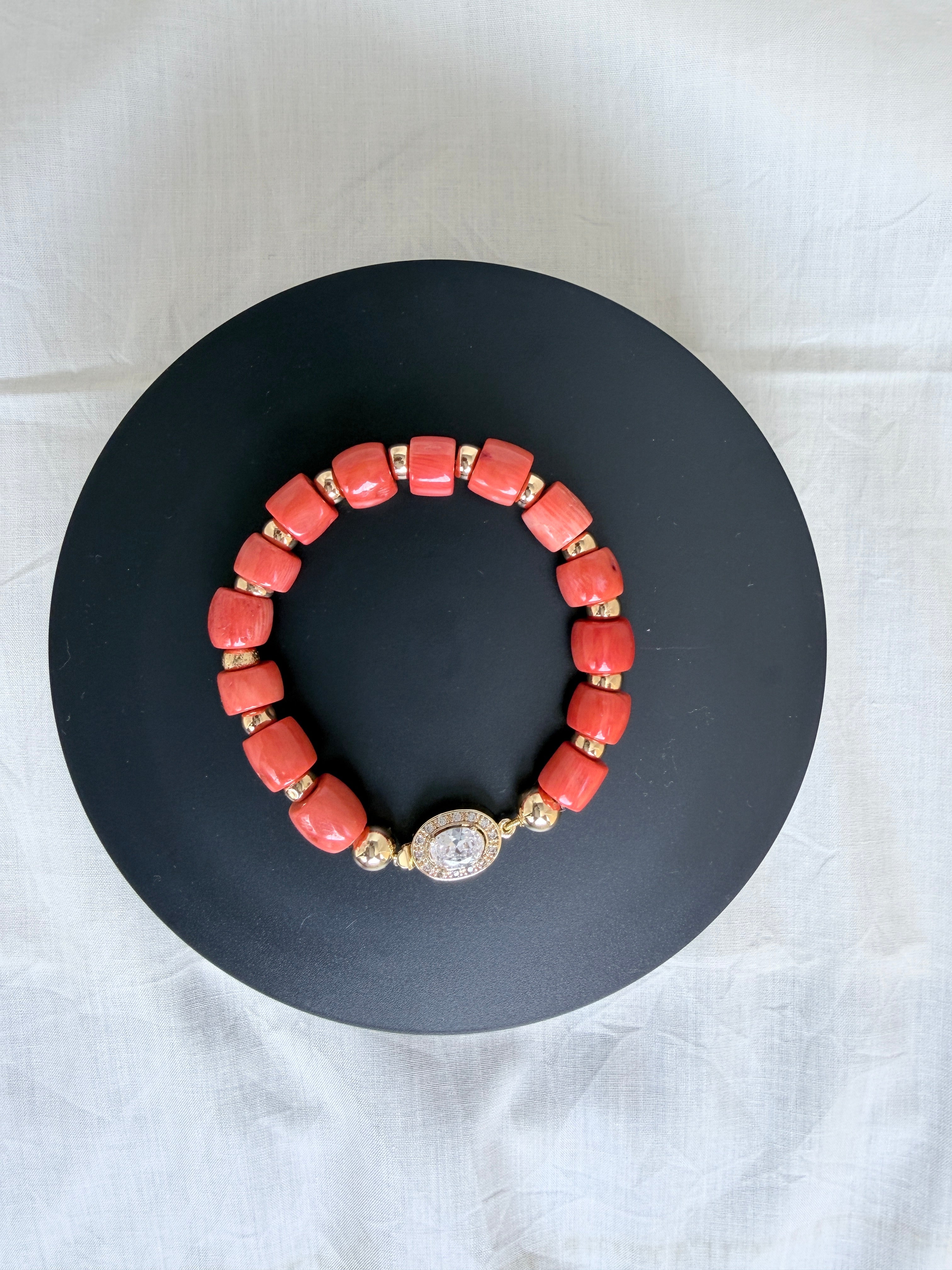 "Coral barrel bead bracelet with oval CZ clasp and gold plated accessories on a black velvet display stand"