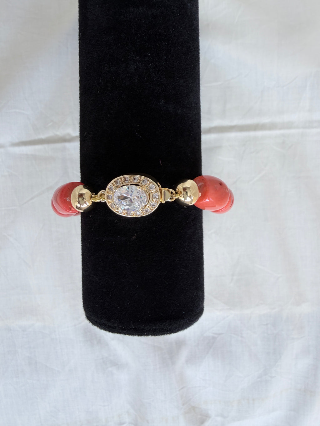 "Coral barrel bead bracelet with oval CZ clasp and gold plated accessories on a black velvet display stand"
