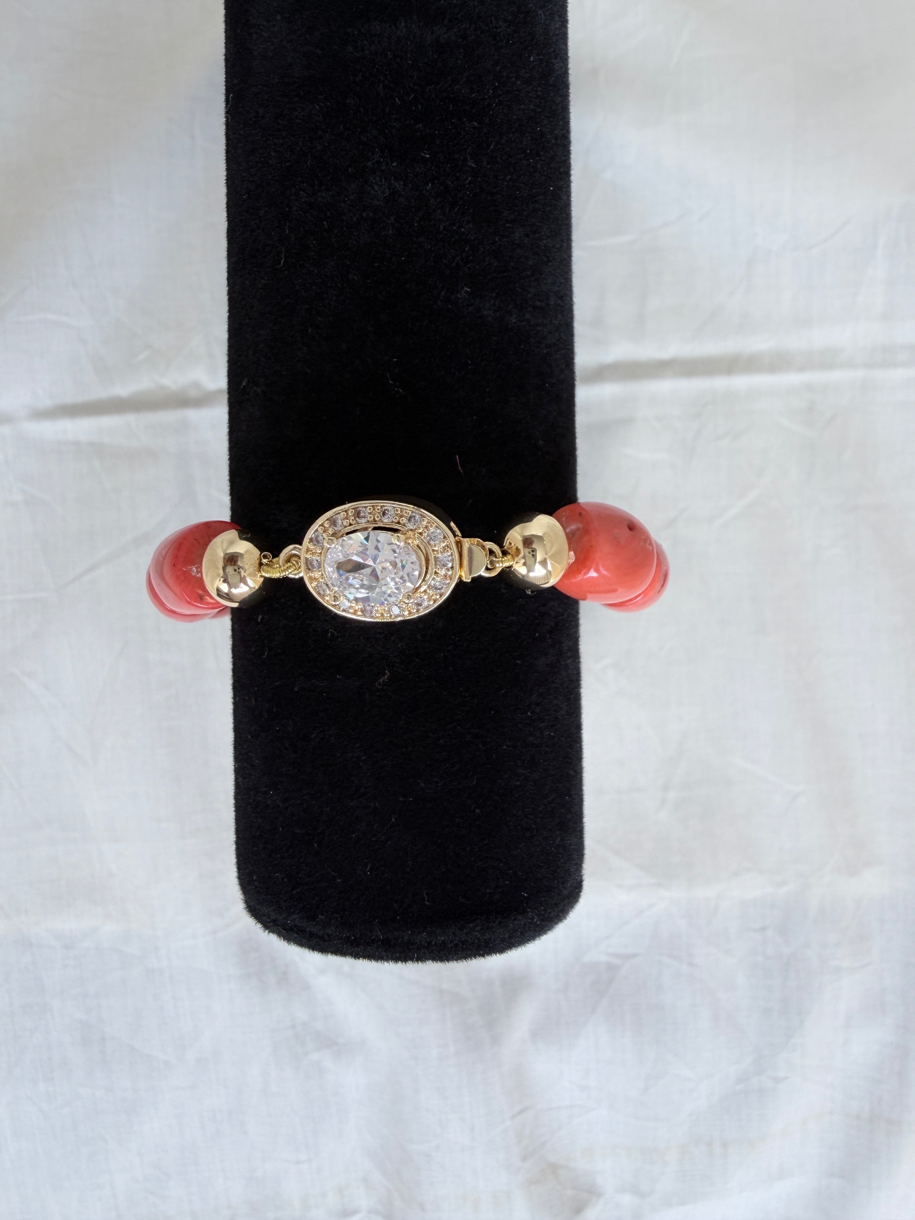 "Coral barrel bead bracelet with oval CZ clasp and gold plated accessories on a black velvet display stand"