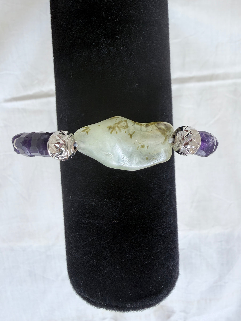 "Close-up of amethyst and green prehnite bracelet on black velvet display stand showing prehnite centrepiece detail"