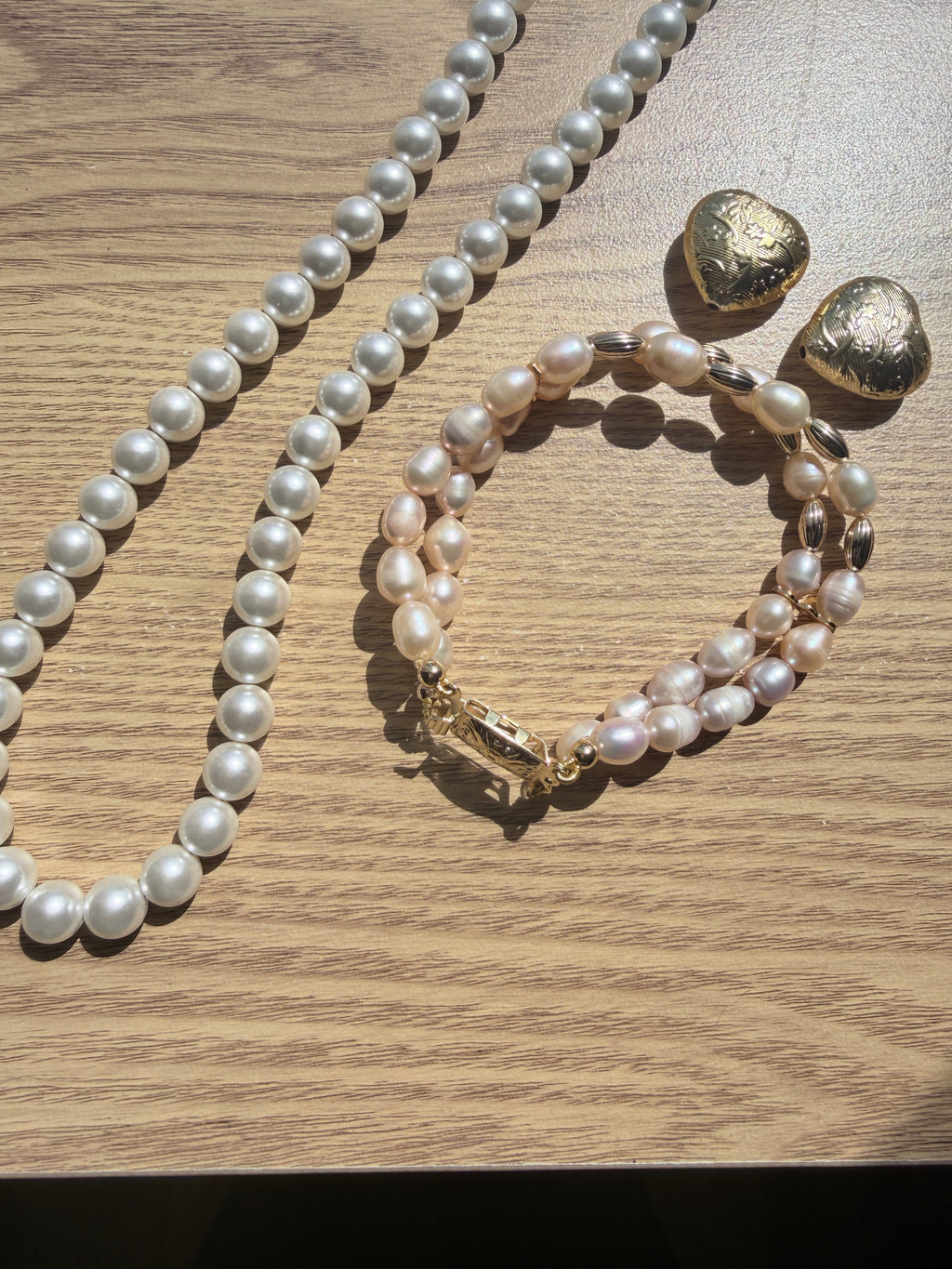 "Lifestyle shot of freshwater pearl two-row bracelet styled with pearl necklace and gold heart accessories on wood surface"