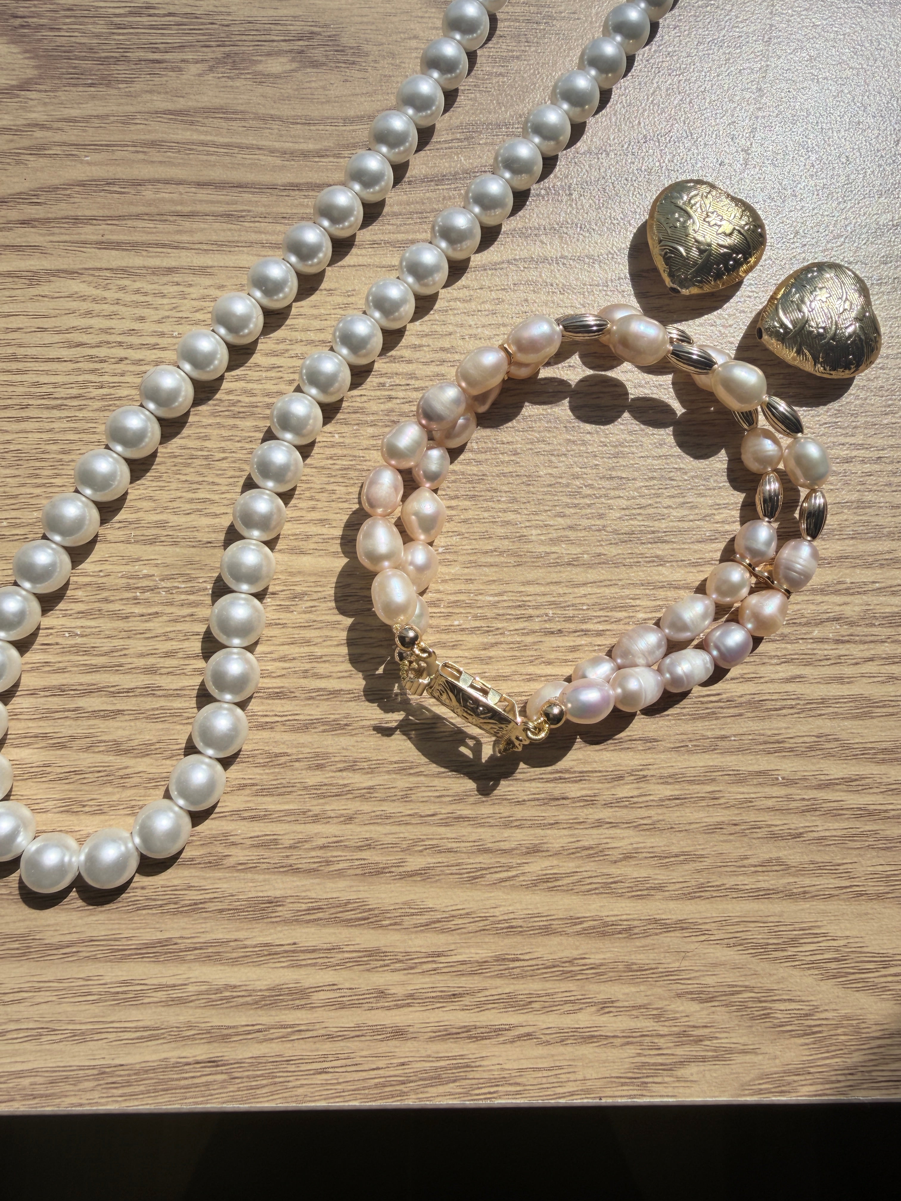 "Lifestyle shot of freshwater pearl two-row bracelet styled with pearl necklace and gold heart accessories on wood surface"