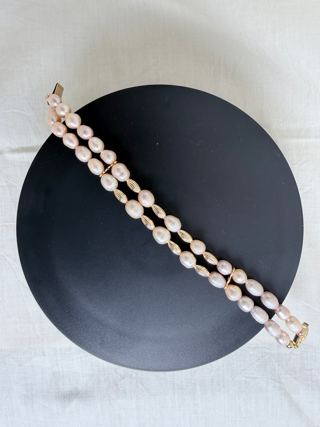 "Freshwater pearl two-row bracelet laid flat on a black circle board showing full bracelet design with gold accessories"