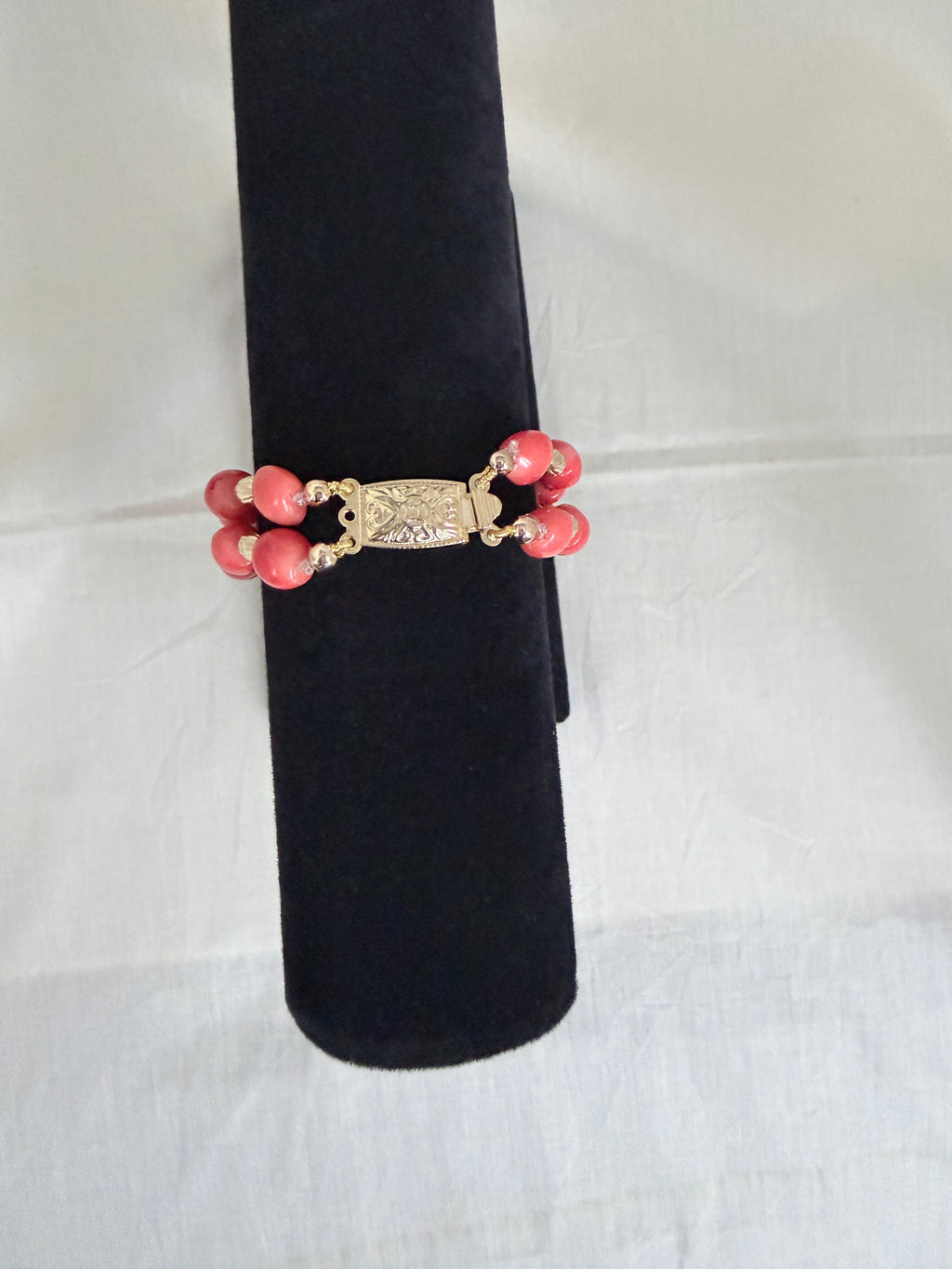"Close-up of barrel coral two-row bracelet on black velvet stand highlighting the decorative gold box clasp"