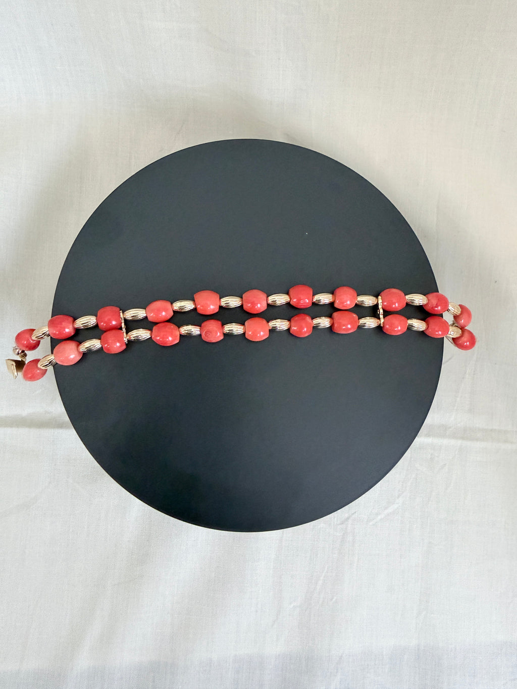 "Barrel coral two-row bracelet laid flat on a dark circle board showing full bracelet design with gold accessories"