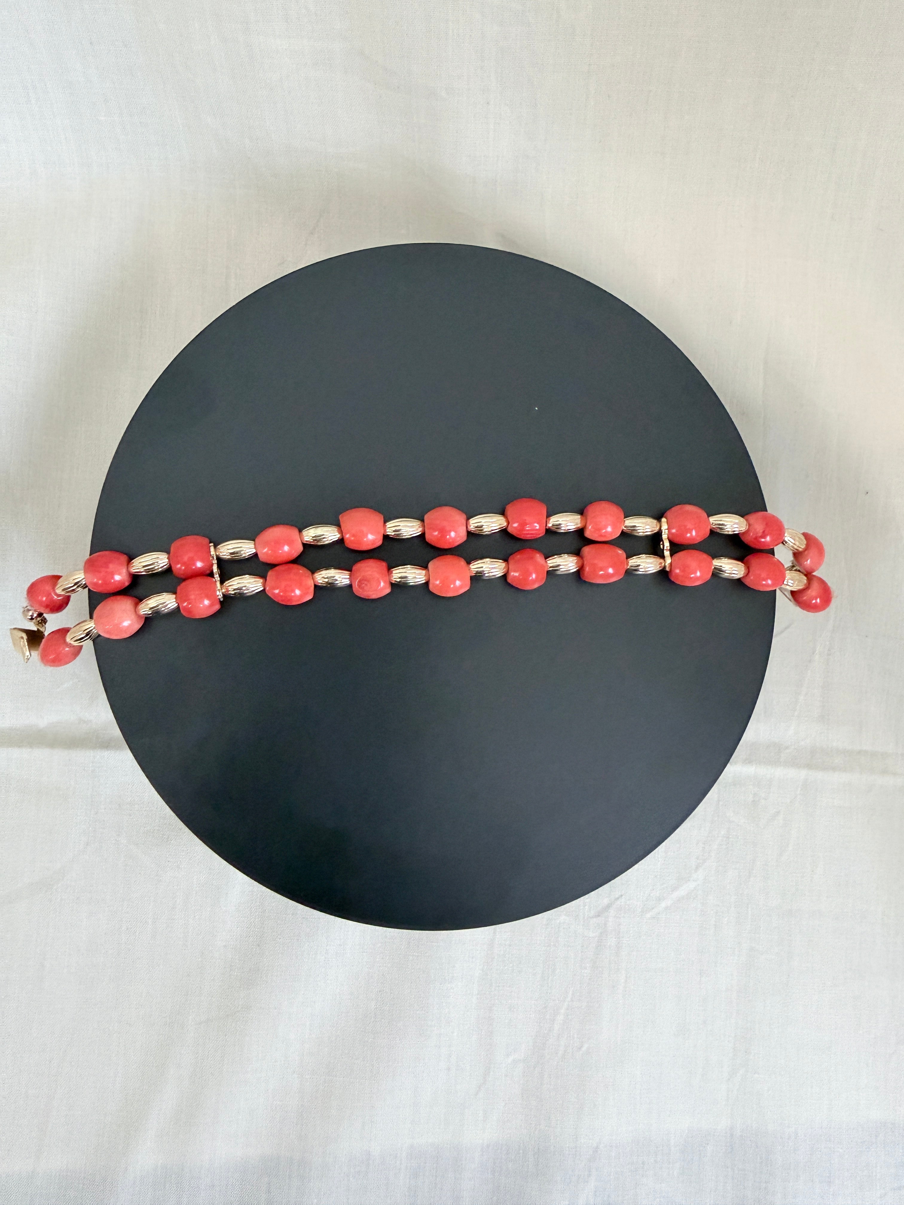 "Barrel coral two-row bracelet laid flat on a dark circle board showing full bracelet design with gold accessories"