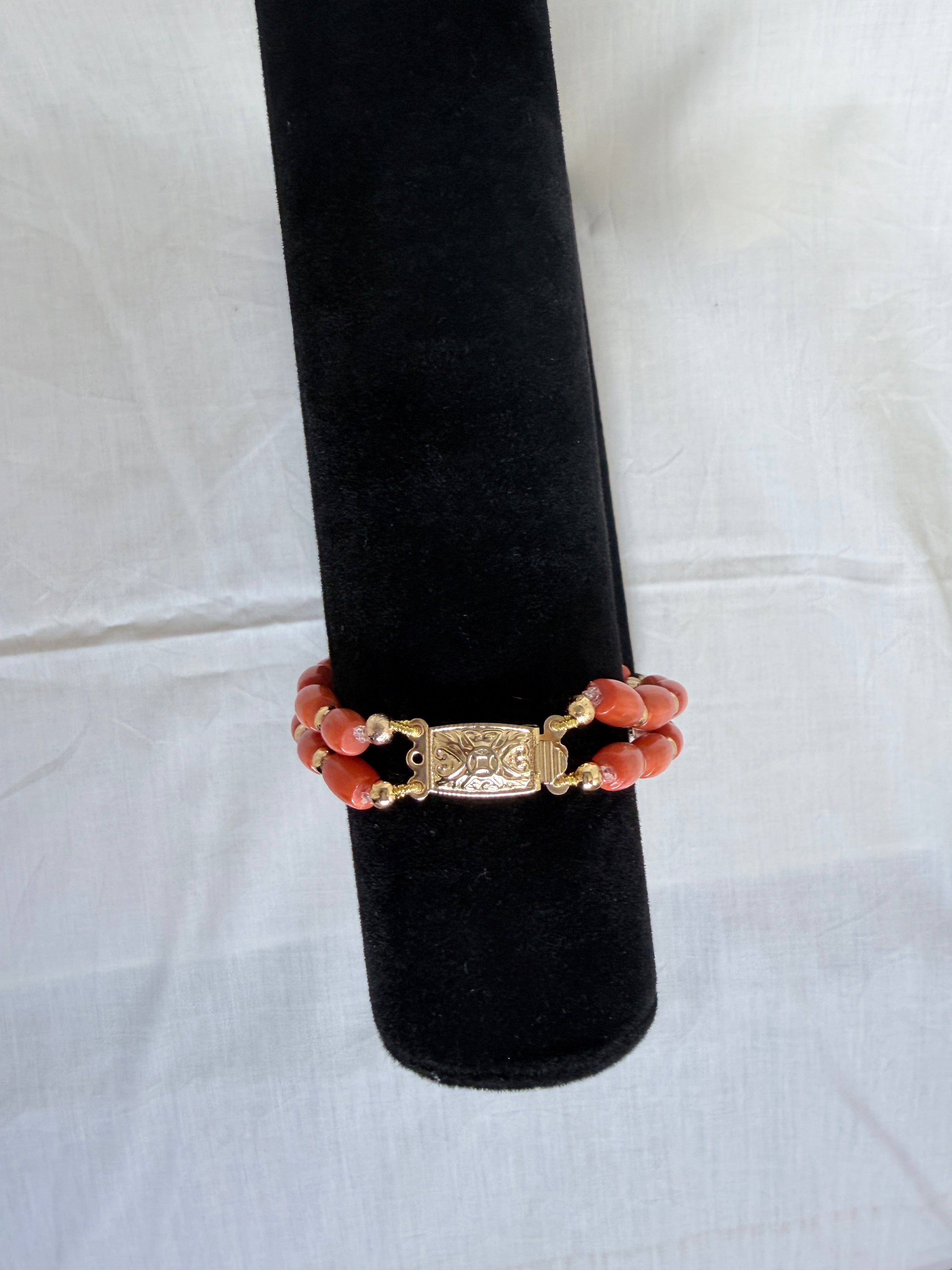 "Close-up of coral tube two-row bracelet on black velvet stand highlighting the decorative gold box clasp"