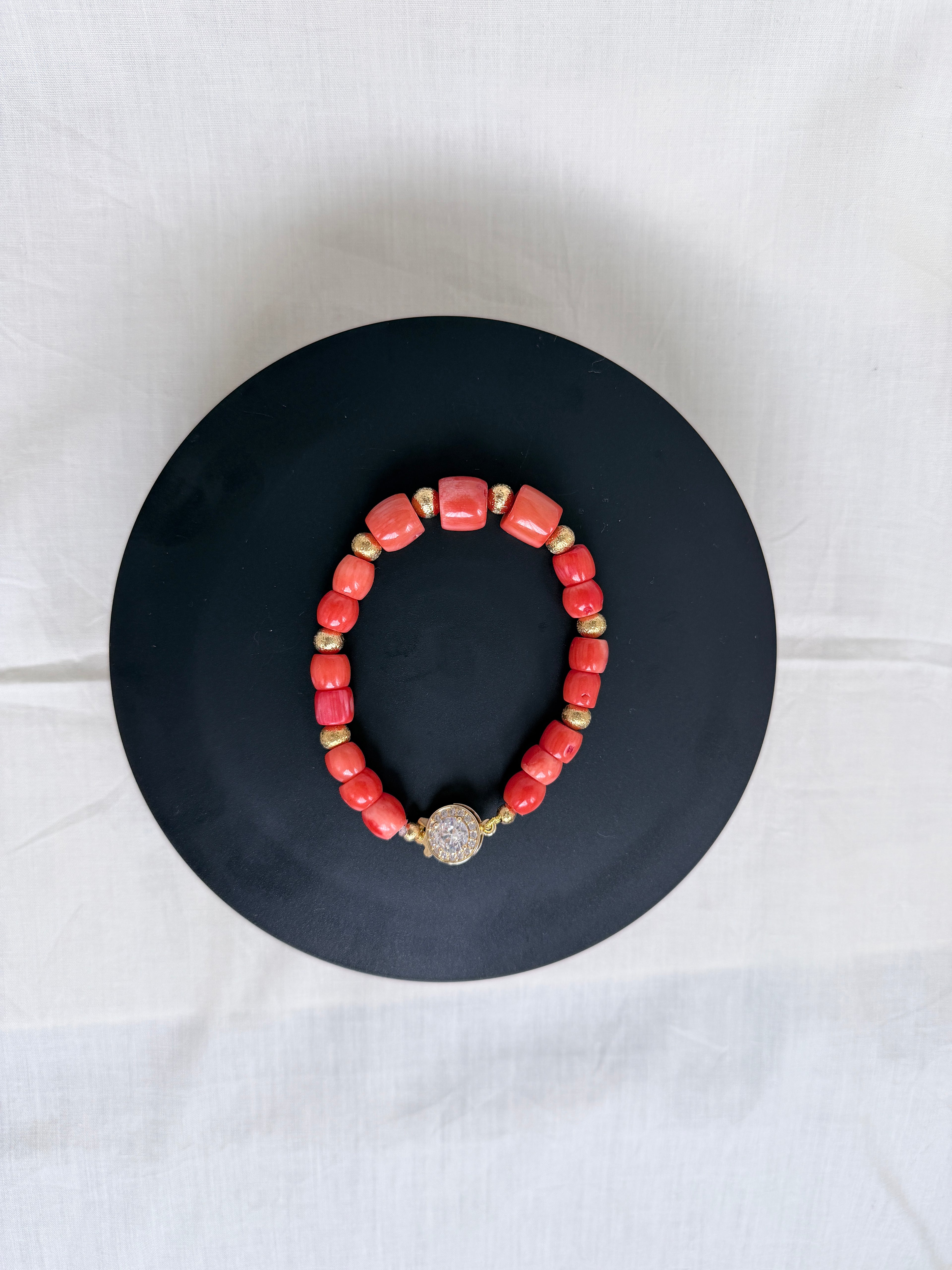"Mixed coral barrel bracelet with CZ fish hook clasp laid flat on a black circle board showing full bracelet and round CZ clasp"