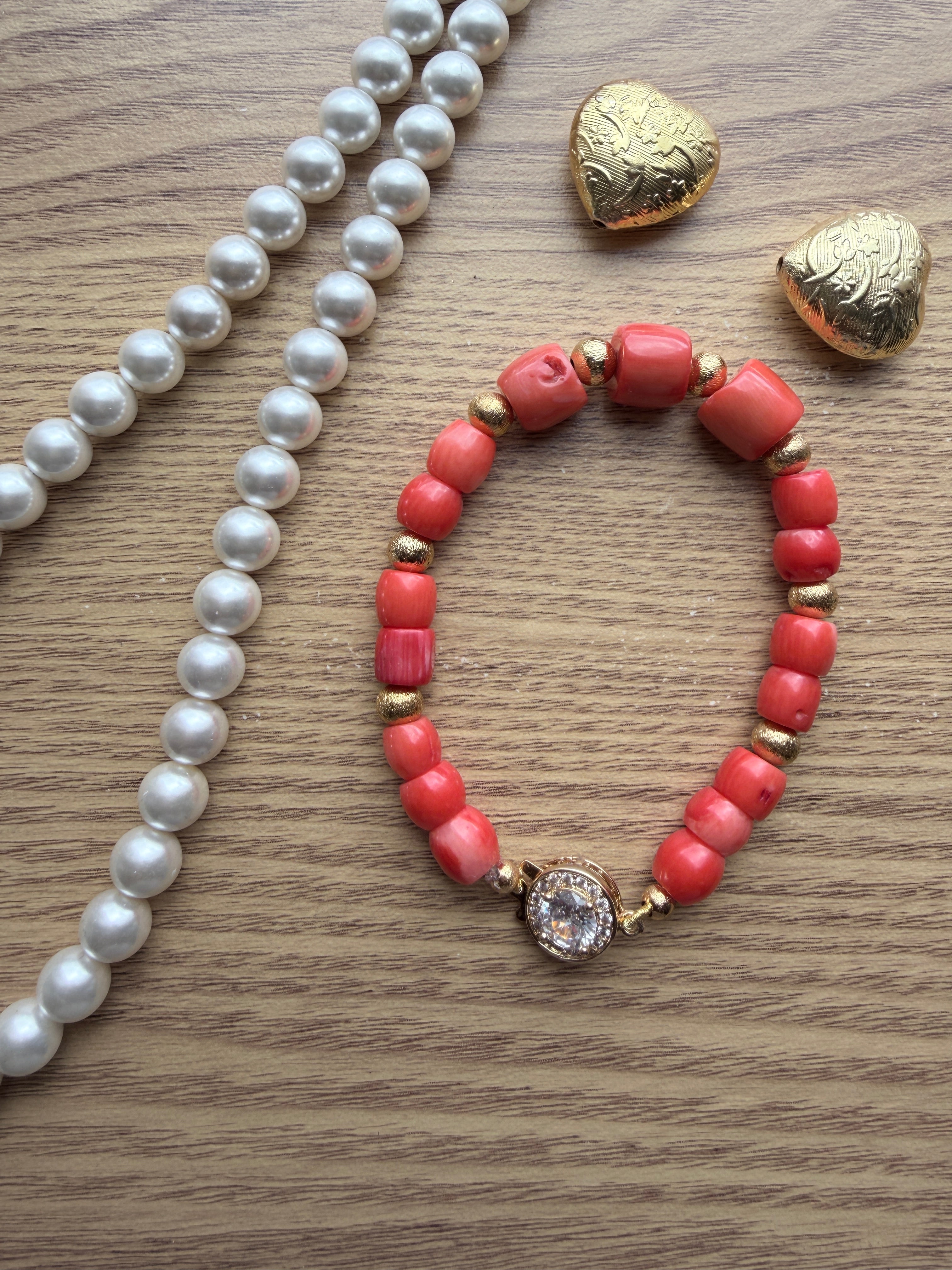 "Lifestyle shot of mixed coral barrel bracelet with CZ fish hook clasp styled with pearl necklace and gold heart accessories on wood surface"