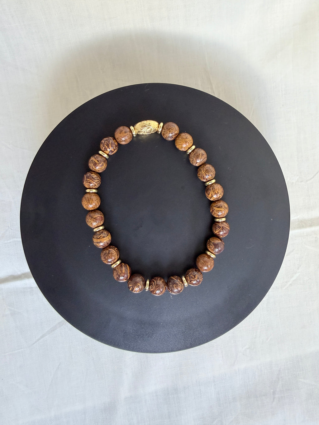"Elephant skin jasper bracelet laid flat on a dark circle board showing full bracelet and ornate gold oval centrepiece bead"