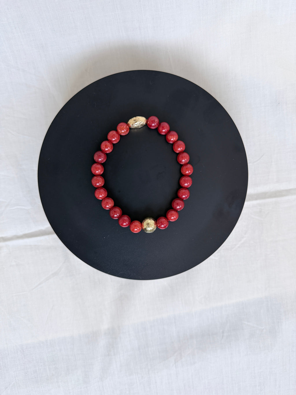  "Coral jade bracelet laid flat on a black circle board showing full bracelet and ornate gold oval centrepiece bead"