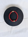  "Coral jade bracelet laid flat on a black circle board showing full bracelet and ornate gold oval centrepiece bead"