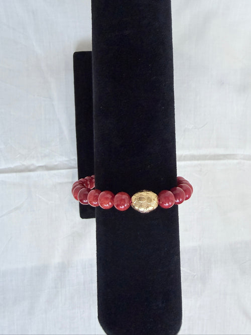 "Coral jade bracelet on black velvet stand showing close-up of ornate gold oval centrepiece bead with round coral jade beads"