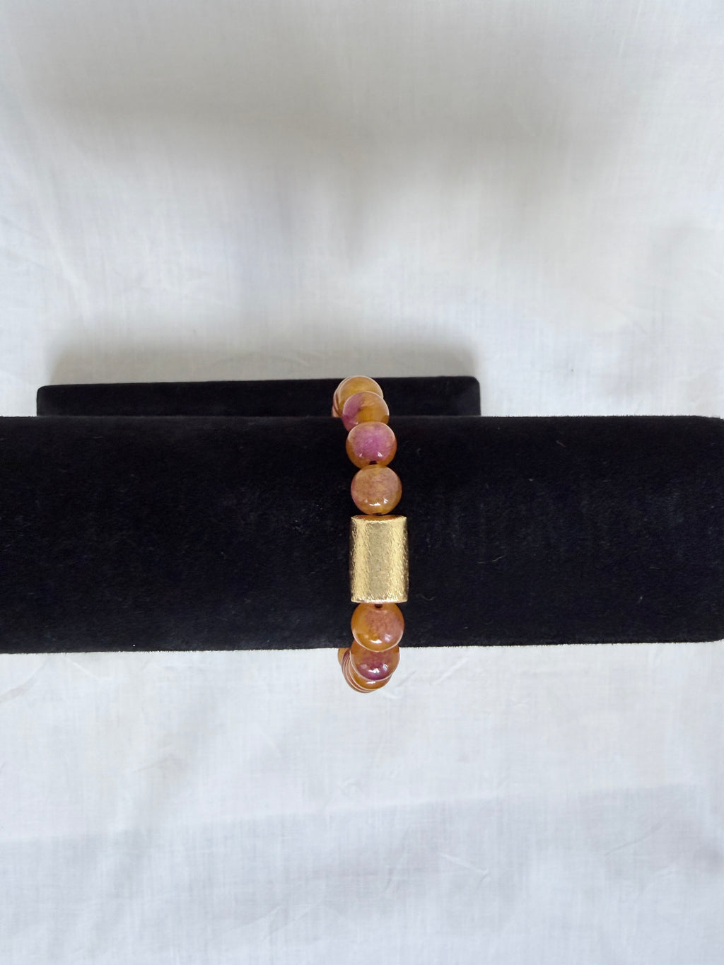 "Multi bronze jade bracelet on black velvet stand showing side view of gold barrel centrepiece with amber and purple jade beads"