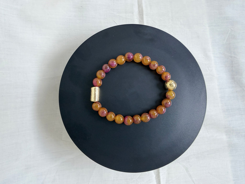 "Multi bronze jade bracelet laid flat on a black circle board showing full bracelet with gold barrel bead and gold round bead accessories"