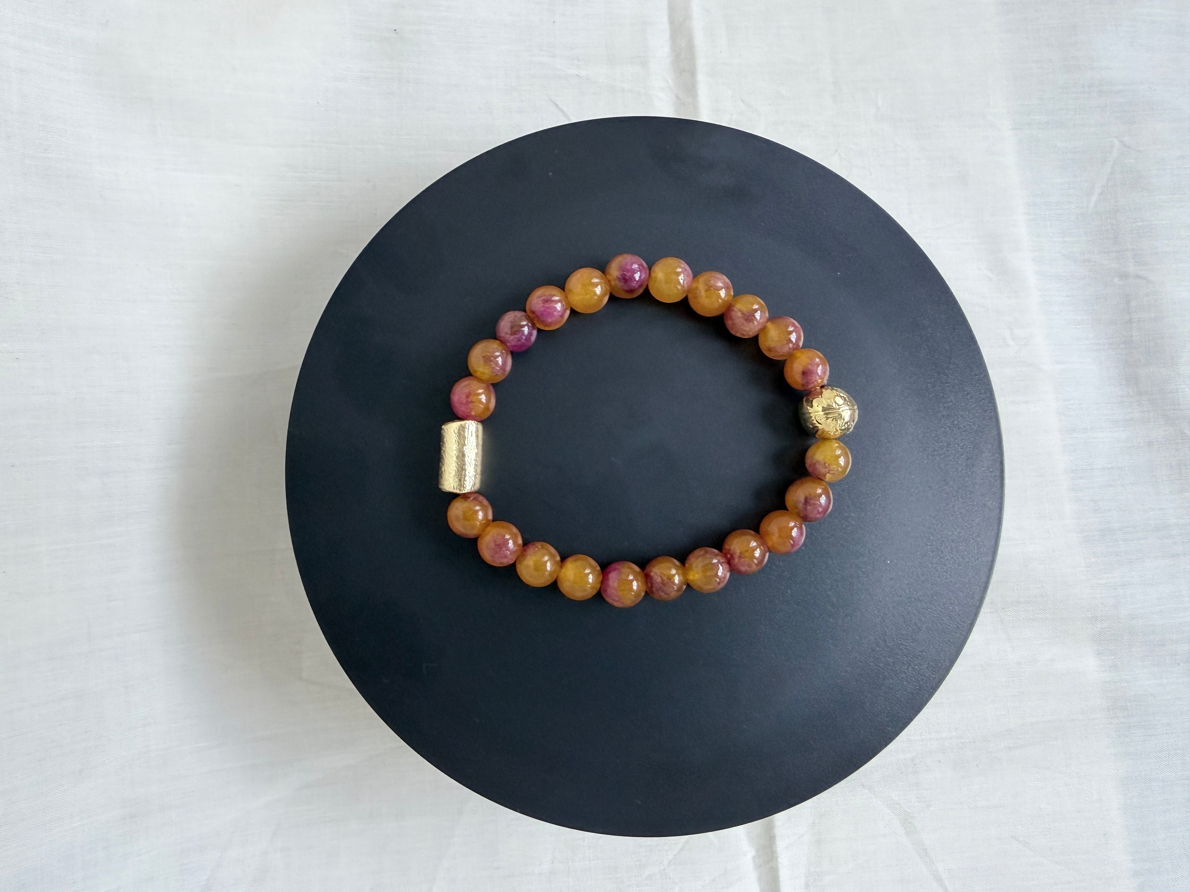 "Multi bronze jade bracelet laid flat on a black circle board showing full bracelet with gold barrel bead and gold round bead accessories"