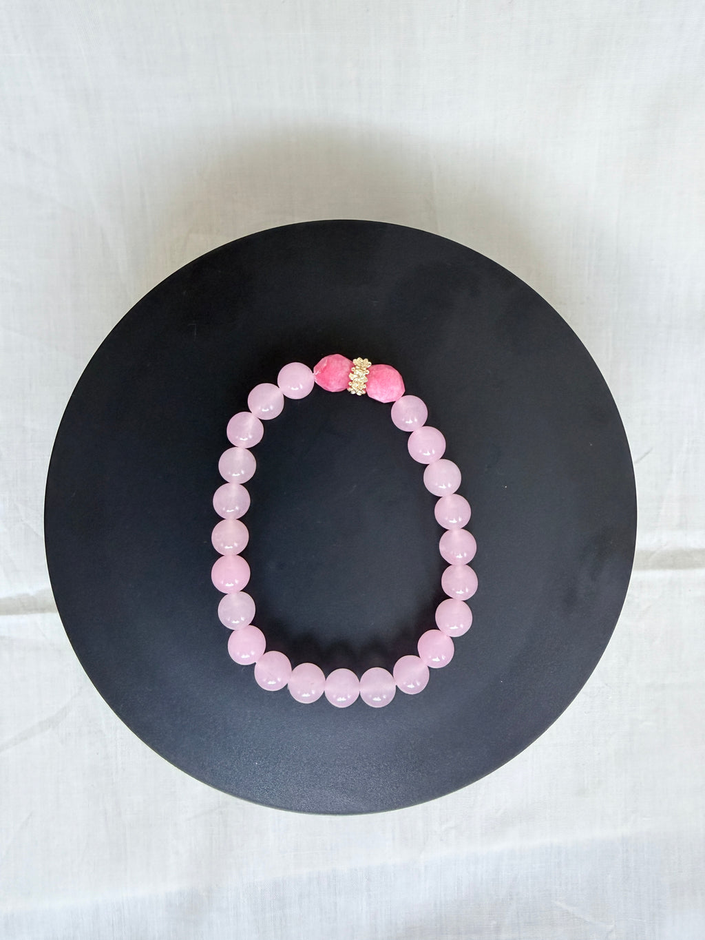 "Pink jade and candy bracelet laid flat on a black circle board showing full bracelet shape and gold rondelle centrepiece"