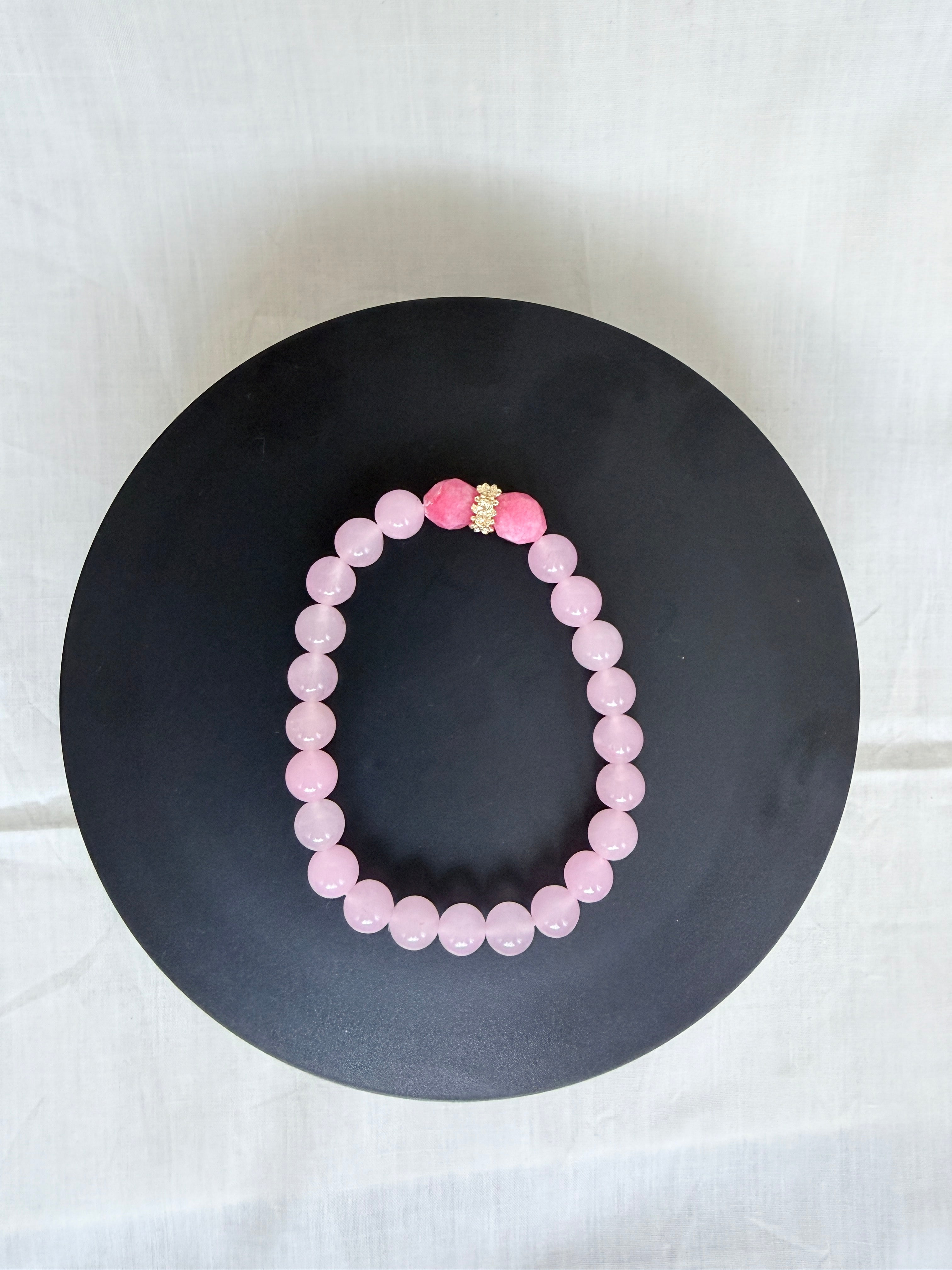 "Pink jade and candy bracelet laid flat on a black circle board showing full bracelet shape and gold rondelle centrepiece"