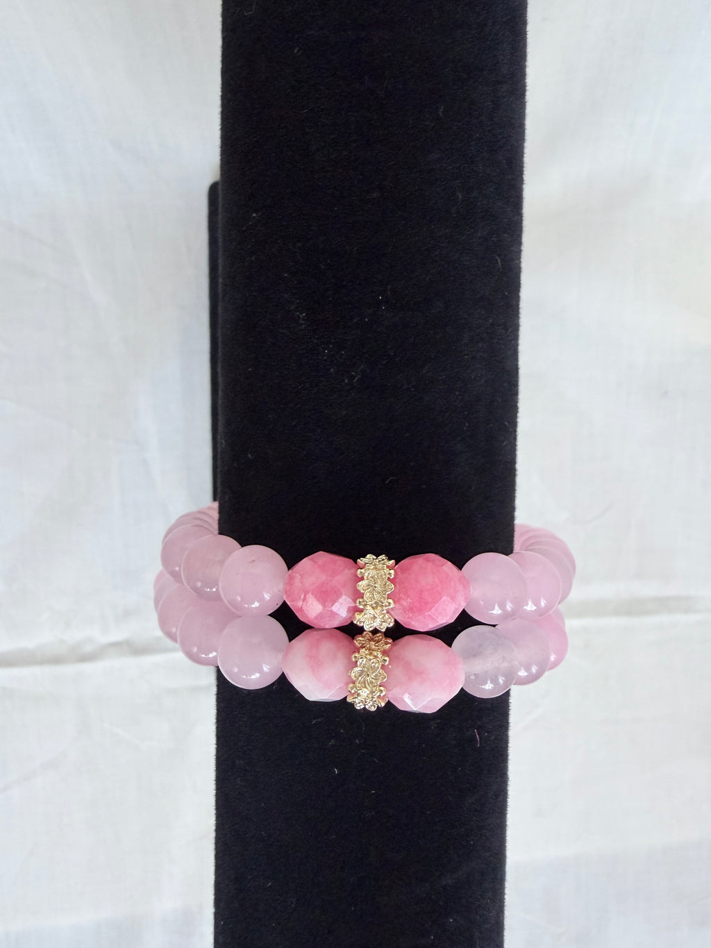 "Two pink jade and candy bracelets stacked on black velvet stand showing how they look layered together with gold  rondelle centrepieces"