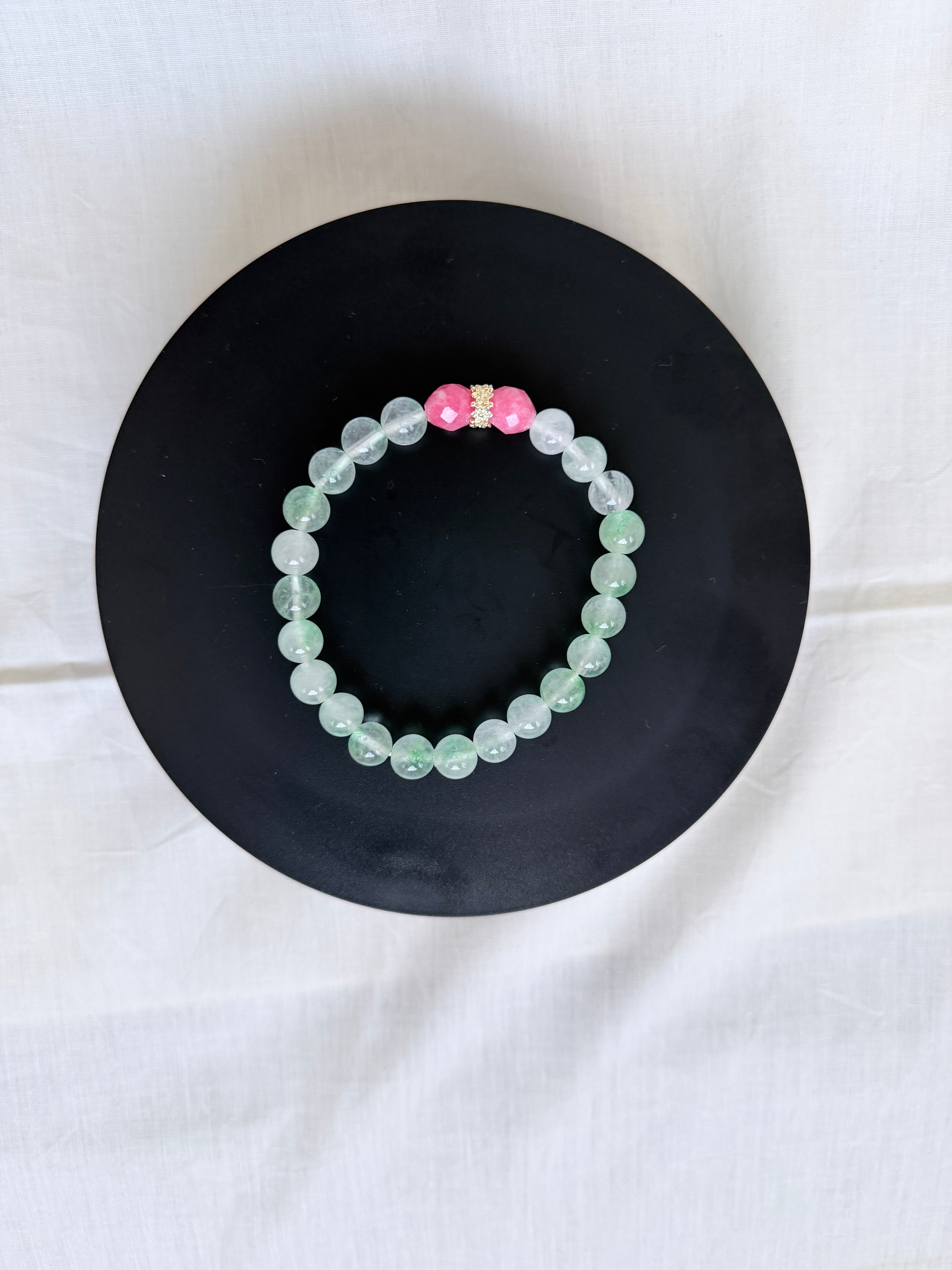 "Mint green jade and candy bracelet laid flat on a black circle board showing full bracelet with pink candy bead and gold CZ rondelle centrepiece"