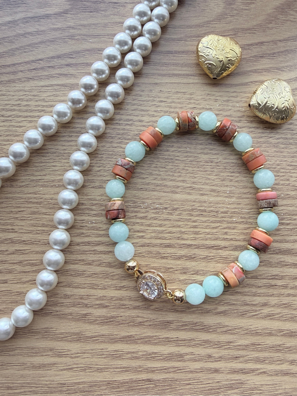 "Lifestyle shot of jasper and aqua agate bracelet styled with pearl necklace and gold heart accessories on wood surface"