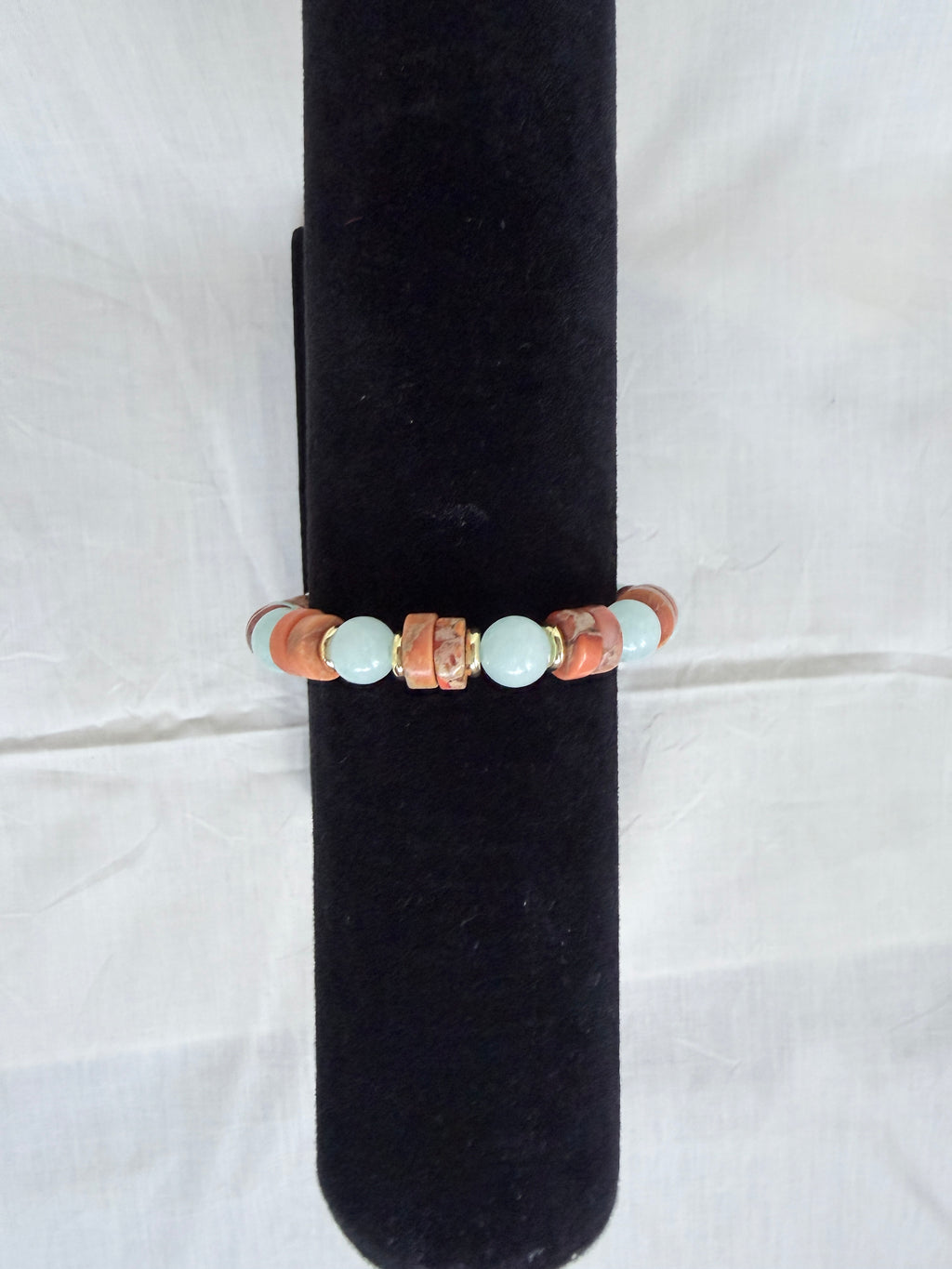 "Jasper and aqua agate bracelet on black velvet stand showing side view of orange-brown jasper wheel beads contrasting with aqua agate beads"