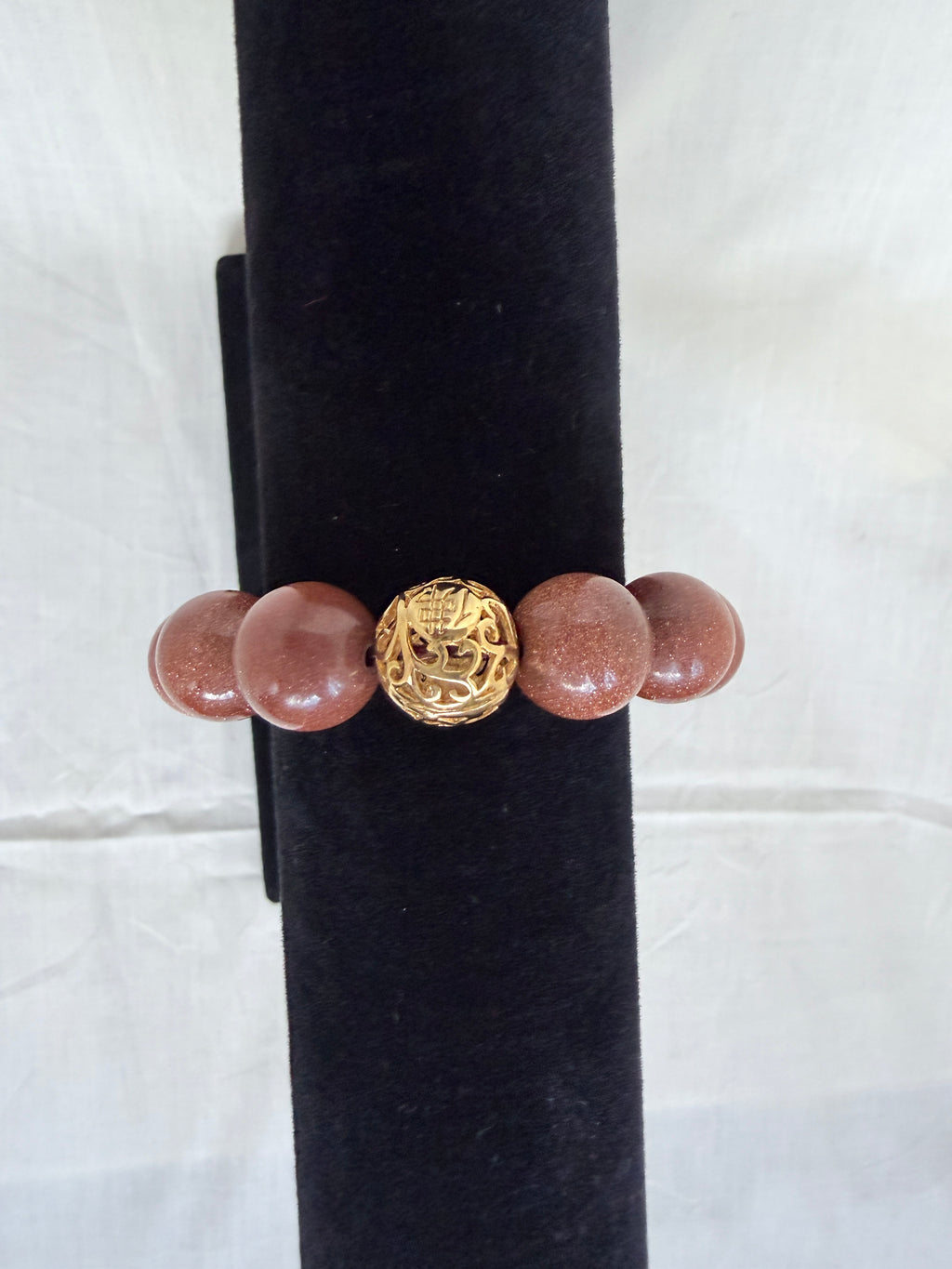 "Brown sandstone bracelet on black velvet stand showing close-up of intricate gold tone filigree focal bead with chunky sparkly brown sandstone beads"