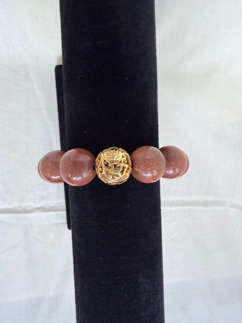 "Brown sandstone bracelet on black velvet stand showing close-up of intricate gold tone filigree focal bead with chunky sparkly brown sandstone beads"