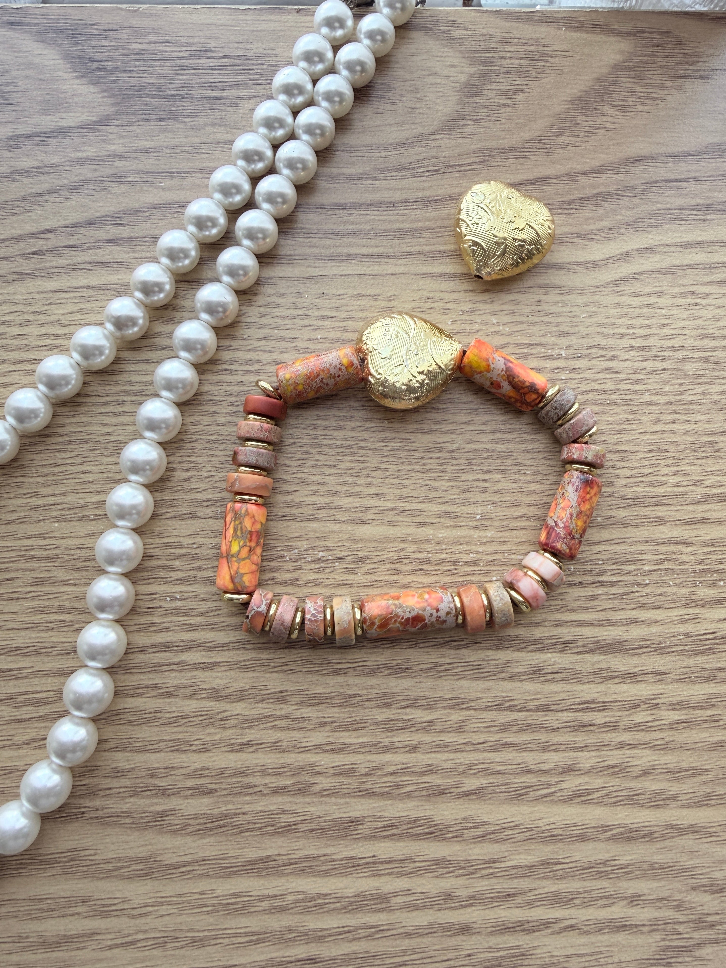 "Lifestyle shot of jasper heart bracelet styled with pearl necklace and gold heart accessories on wood surface"