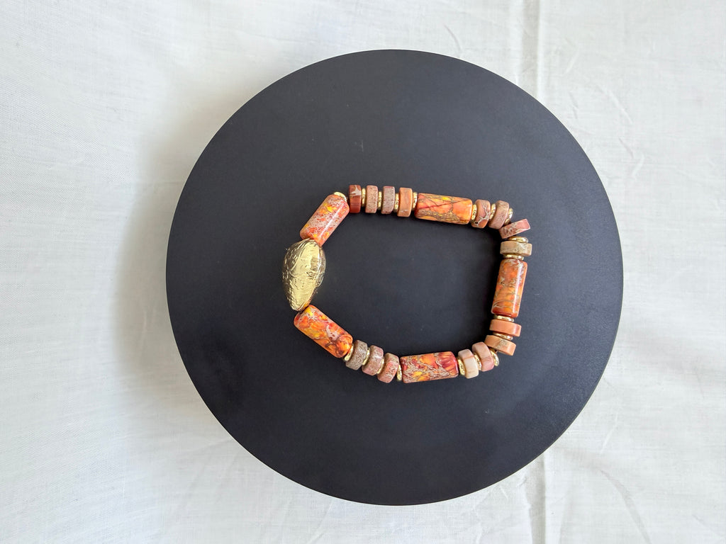 "Jasper heart bracelet laid flat on a black circle board showing full bracelet with multi-colour orange terracotta jasper tube and wheel beads and engraved brass heart focal bead"