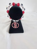 Money Moves Charm Bracelet on black velvet stand showing silver CZ dollar sign charm with red rhinestones and raspberry and crystal rondelle beads