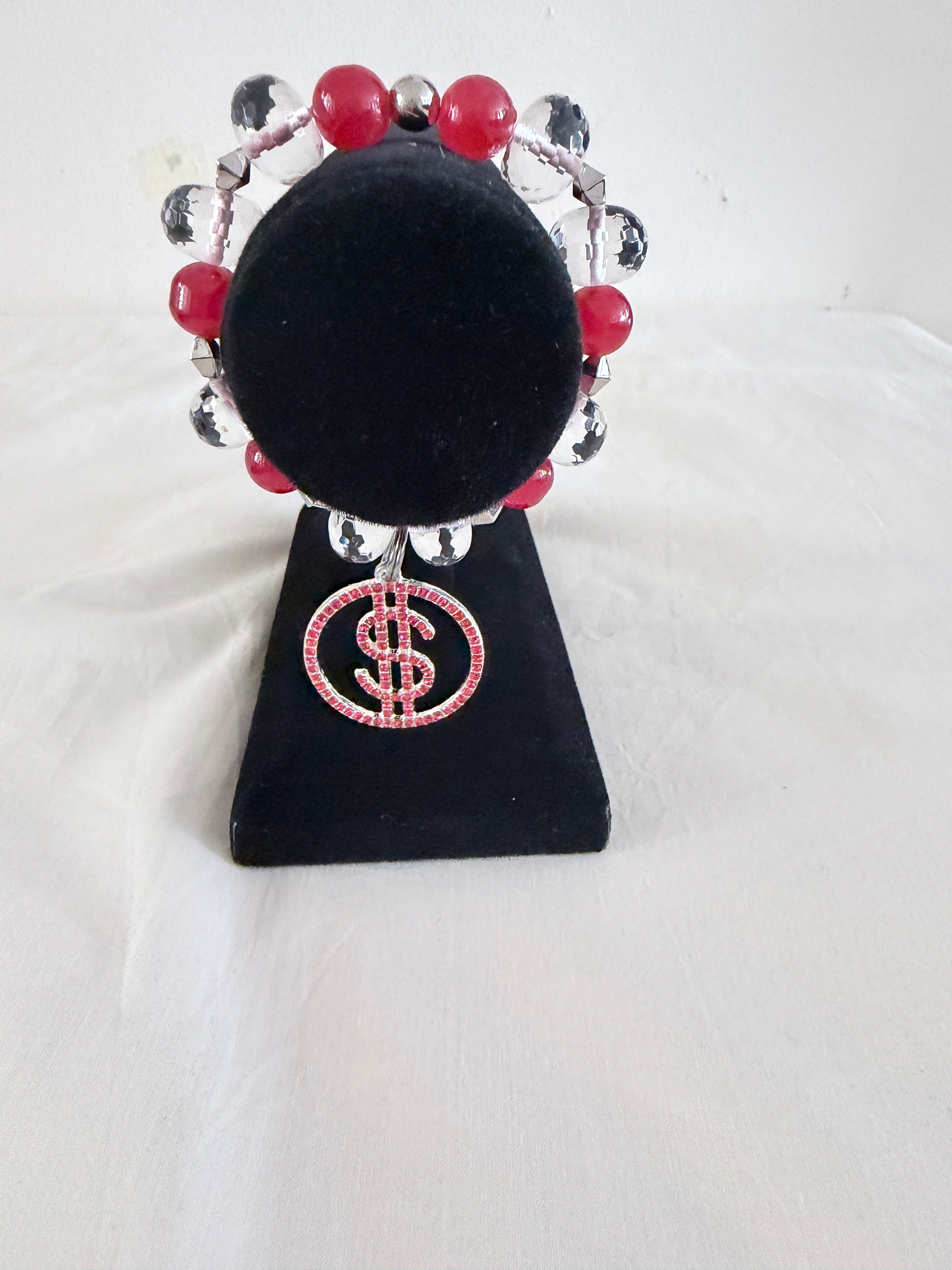 Money Moves Charm Bracelet on black velvet stand showing silver CZ dollar sign charm with red rhinestones and raspberry and crystal rondelle beads