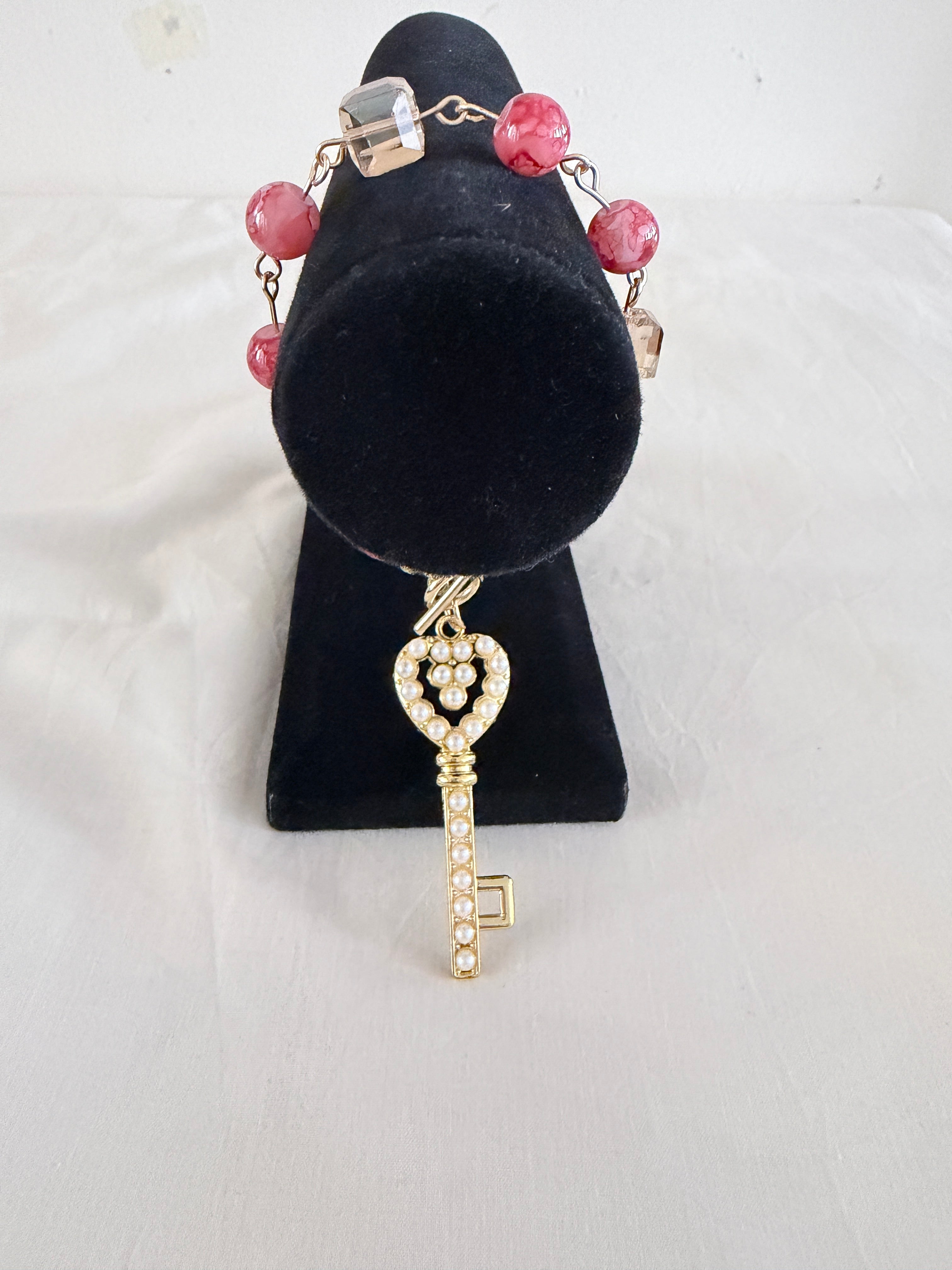 Key to My Heart Charm Bracelet on black velvet stand showing large pearlised gold key charm with mottled pink orange and champagne cube beads on linked chain