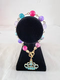 Queen of Everything Charm Bracelet on black velvet stand showing teal rhinestone gold crown charm with multicolour pink purple lavender and teal beads on gold link chain