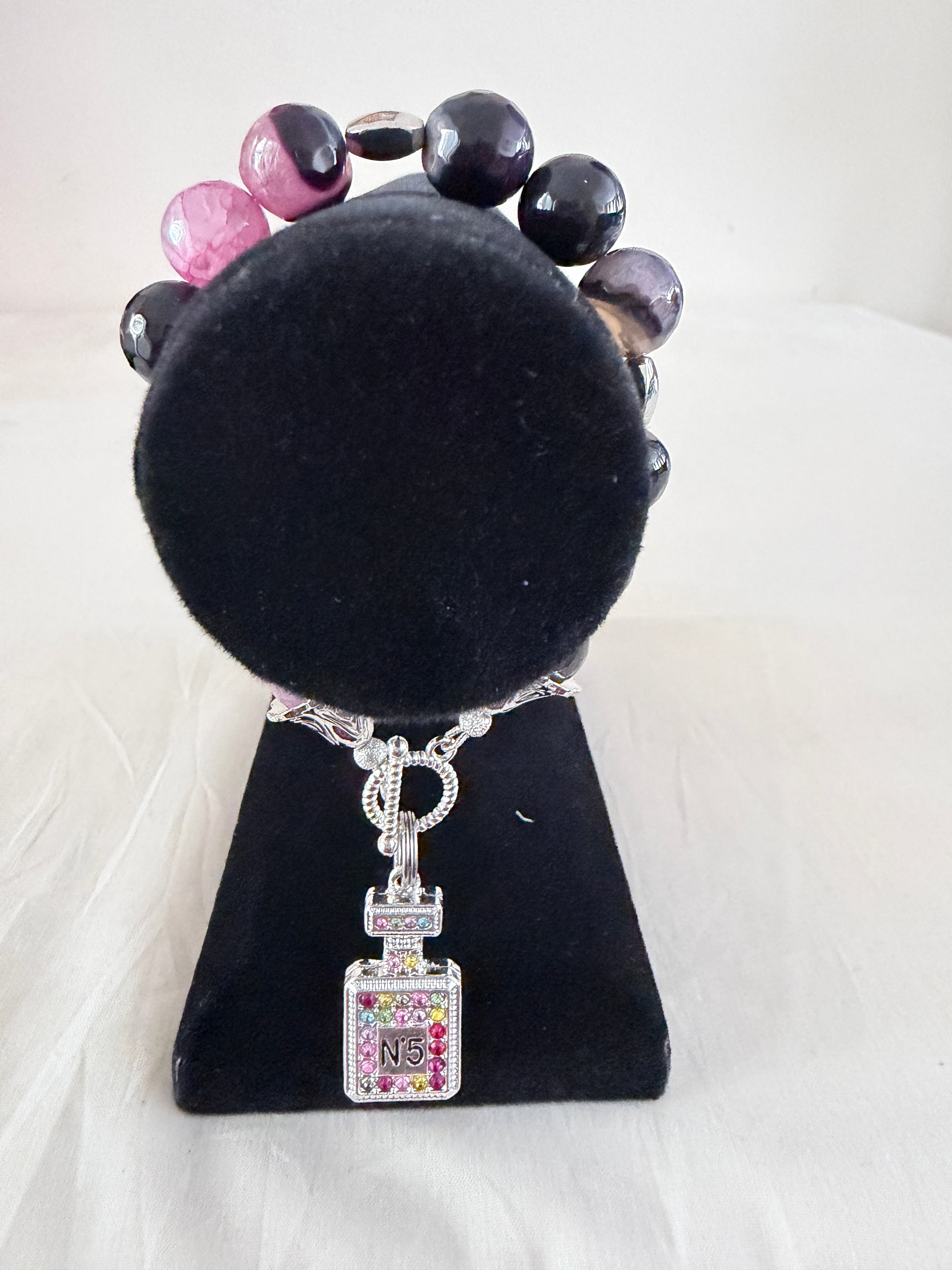 Scent of Luxury Charm Bracelet on black velvet stand showing multicolour rhinestone silver perfume bottle charm with purple banded agate beads and silver bell end caps