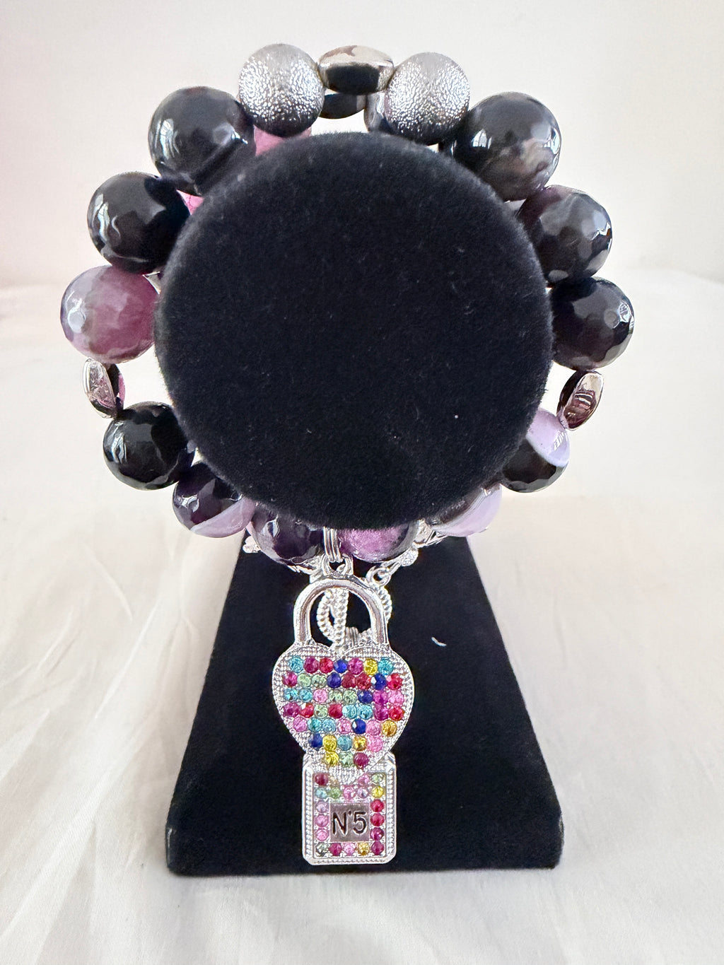Scent of Luxury Charm Bracelet on black velvet stand close up showing multicolour rhinestone perfume bottle and heart charm detail with purple agate and silver stardust beads