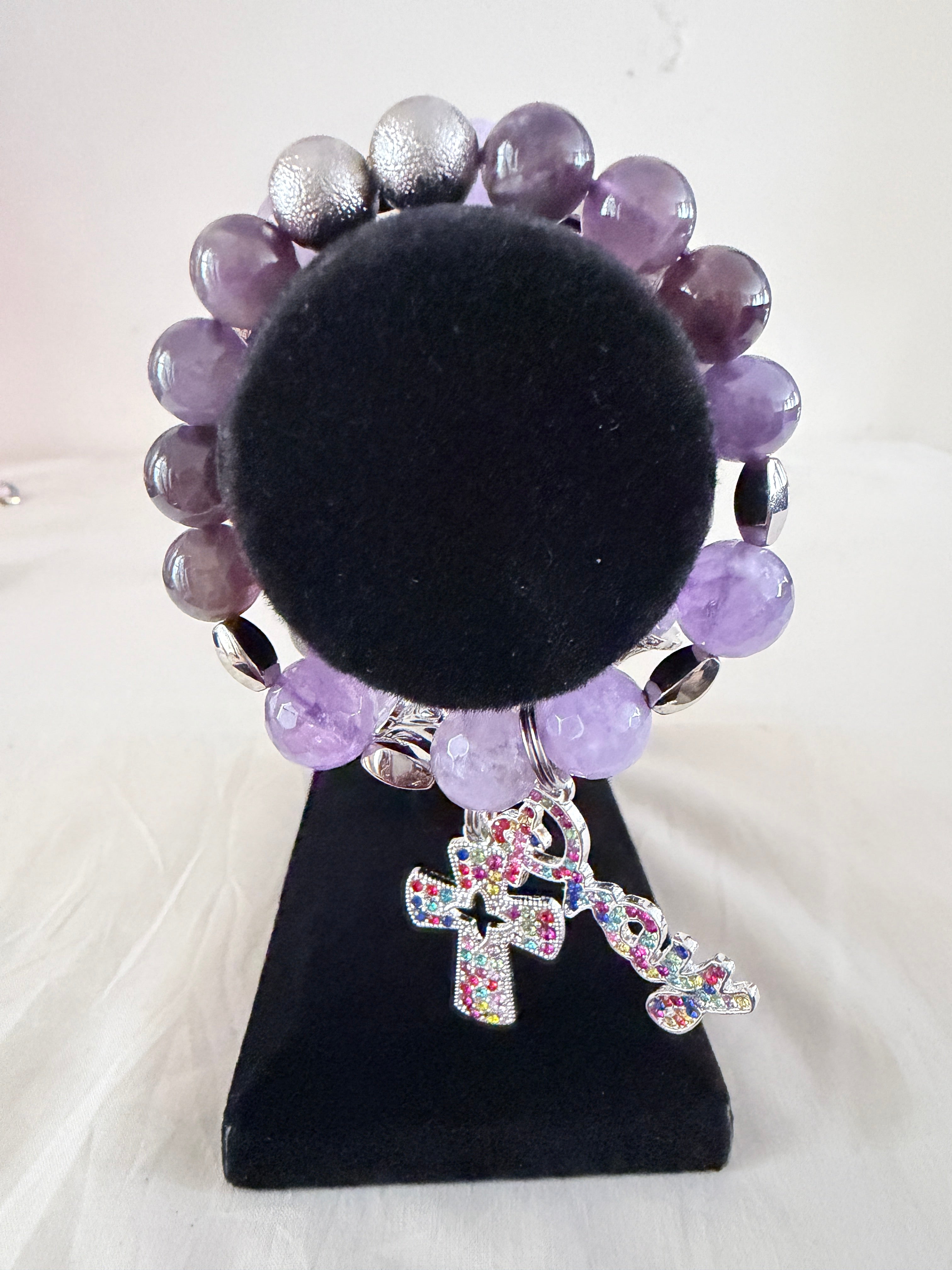 Holy Grace and Faith & Grace Charm Bracelets on black velvet stand showing multicolour rhinestone cross and Pray script charms with natural amethyst and silver stardust beads