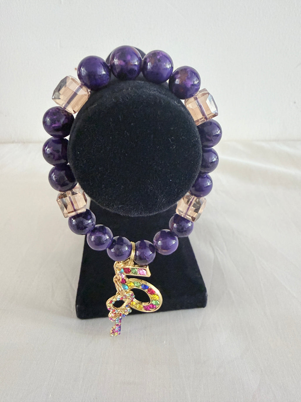 Purple bead and champagne cube crystal charm bracelet displayed on black jewellery stand