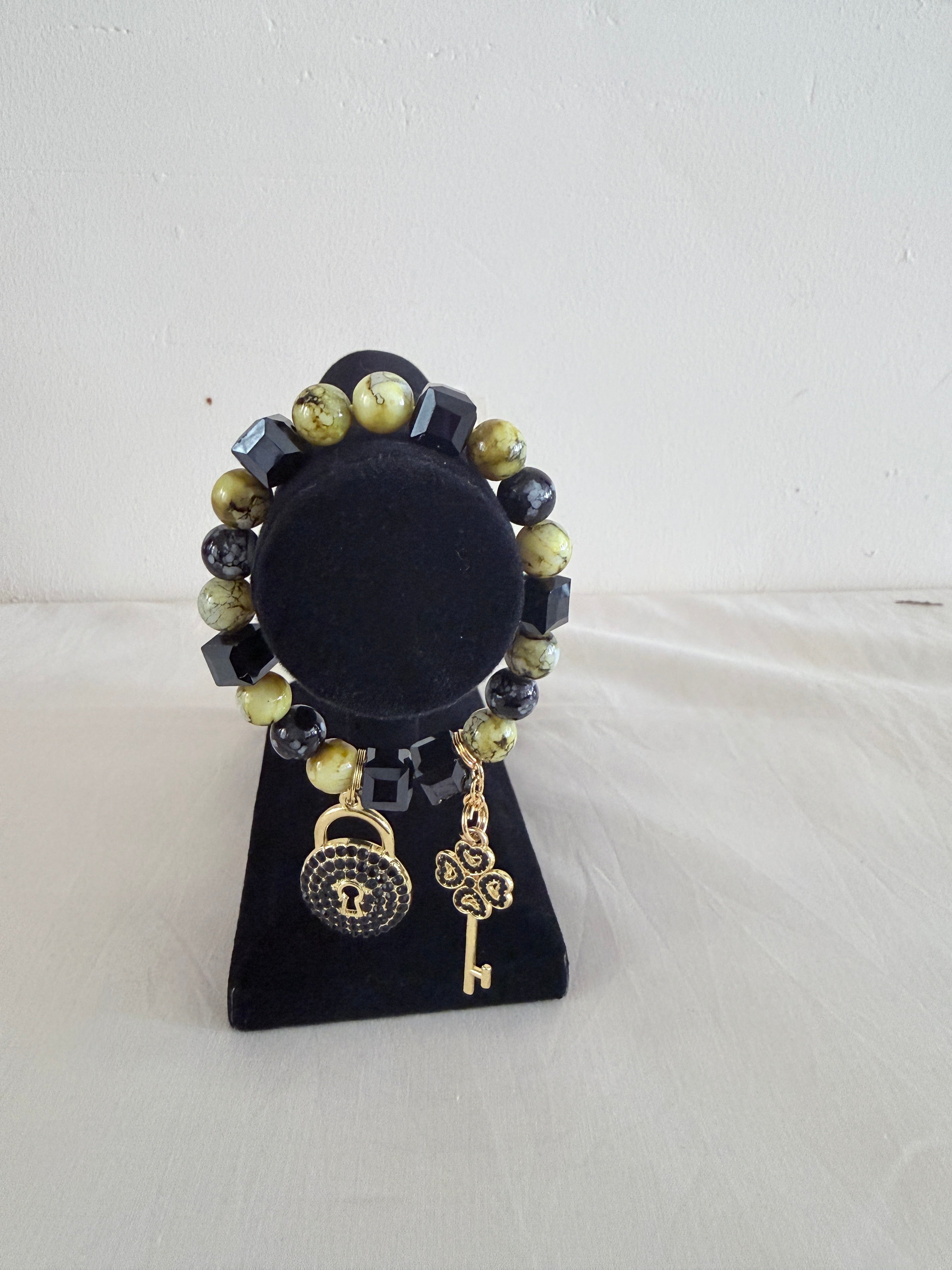 Lime and black cube bead bracelet with gold lock and key charms on black jewellery stand