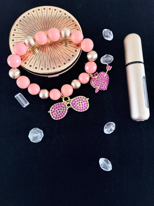 Blush pink and gold bead bracelet with purple rhinestone sunglasses and heart arrow charms flat lay on dark background - LoyatobsCreations.com