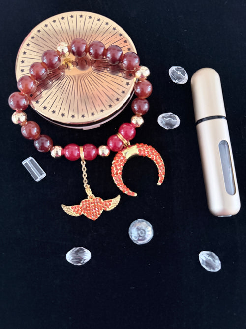 Burgundy ceramic bead bracelet with gold rhinestone crescent moon and winged heart charms flat lay on dark background - LoyatobsCreations.com