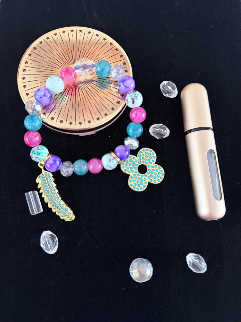 Multicolour mixed bead bracelet with gold turquoise rhinestone flower and feather charms flat lay on dark background - LoyatobsCreations.com